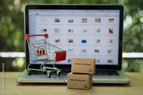 Miniature cardboard boxes with shopping cart and laptop computer background