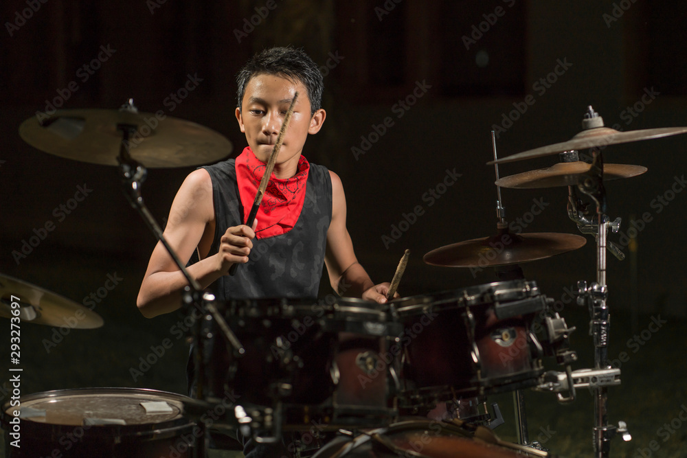 Naklejka premium Asian American mixed teenager playing drums at home garden . cool and handsome young boy practicing on drum kit rehearsing passionate in badass rock band look