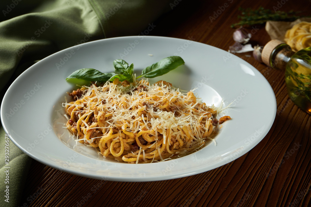 Bolognese pasta with red sauce, parmesan and minced meat. Italian spaghetti with meat in a white plate on a wooden background.