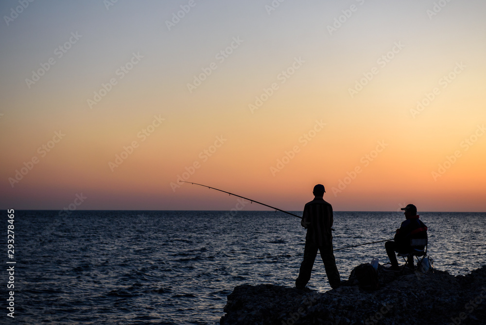 Sea, sunset, and the silhouette of a fisherman-the silhouette of a man with a fishing rod on the background of the setting sun over the sea.