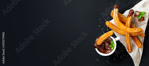 Churros with a cup of hot chocolate on black background. top view. Churro sticks closeup. photo