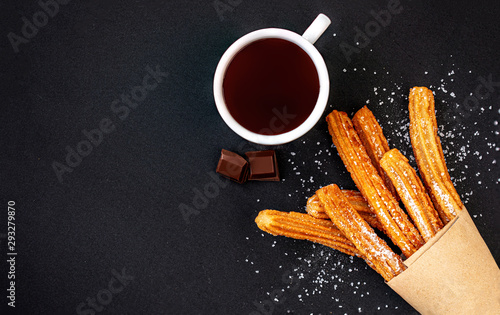 Churros with sugar and chocolate sauce on black background. top view. Churro sticks in a paper bag..