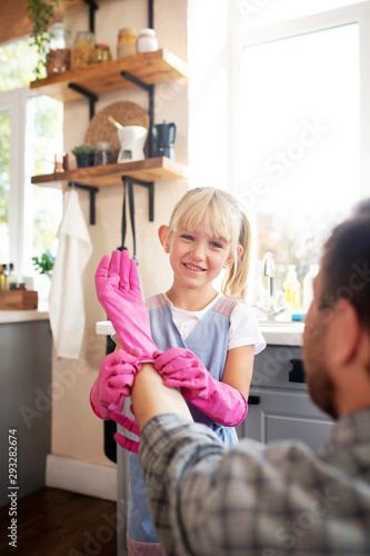 Cheerful blonde daughter helping father to put glove on