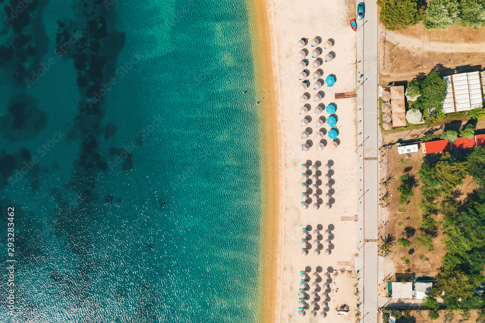 Aerial view from a drone to the sea sandy beach with sun beds and umbrellas for tourists in Greece. Turquoise clear water on the beach on a sunny summer day. Tourist season
