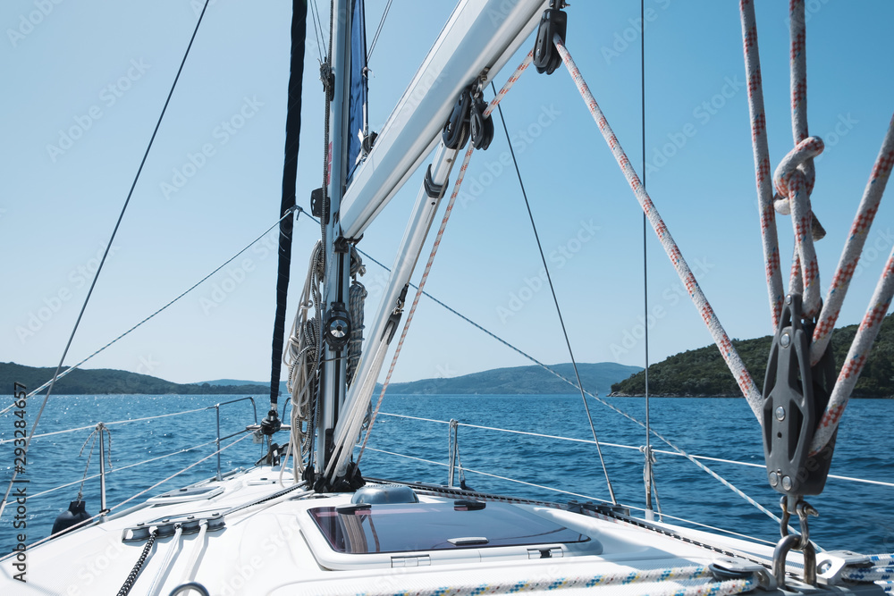 Bow of yacht and yacht equipment. The texture of the masts and ropes on a background of mountain peaks, blue sea and blue sky on a sunny day in summer. Details of sailing equipment. Tourism. Travel