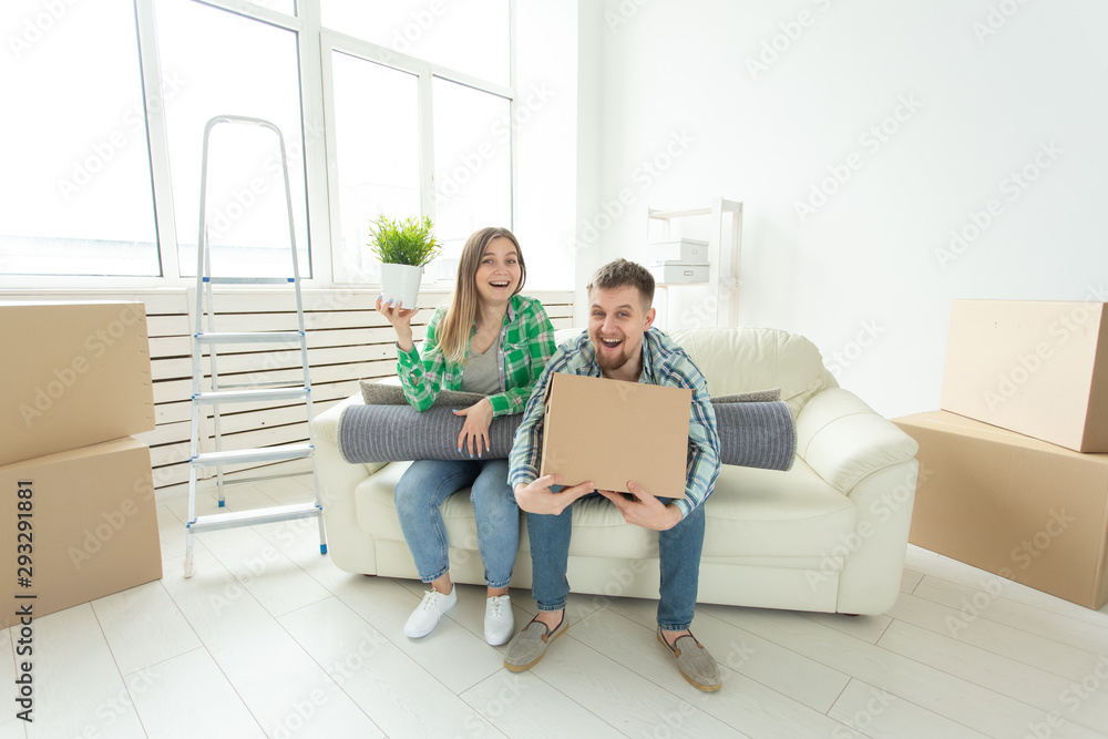 Cheerful joyful young couple charming girl and handsome man holding a box with things and a pot with a plant while moving to a new apartment. Housewarming and mortgage concept.