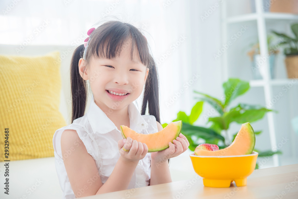 Little asian girl holding a slice of japanese melon and smiles at home Little asian girl holding a slice of japanese melon and smiles at home