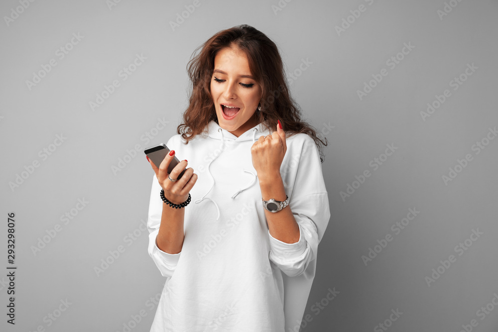 Happy young woman showing victory sign over gray background Happy young woman showing victory sign over gray background