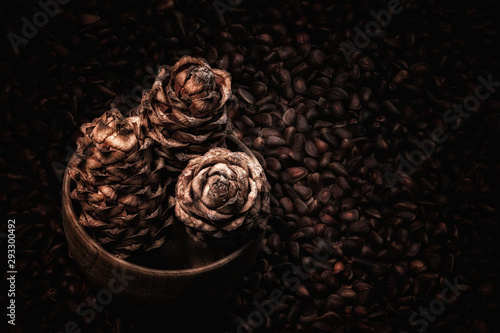 three cedar cones in a wooden cedar bowl on a background of pine nuts