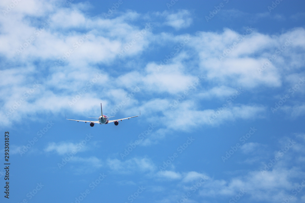 Airplane flying in the blue sky on background of white clouds, rear view. Two-engine commercial plane during the turn, turbulence and travel concept