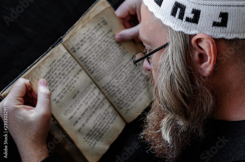 A Hasidic Jew reads Siddur. Religious orthodox Jew with a red beard and with pace in a white bale praying. On the bale is an inscription Rabbi Nahman from Uman. Closeup photo