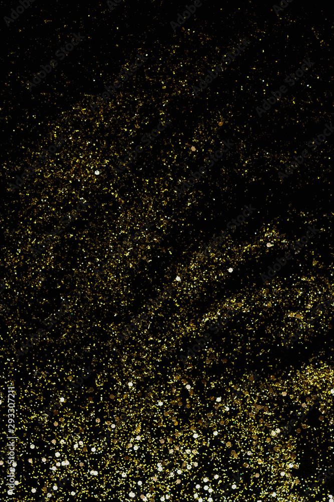 Golden glitter scattered on the black card background, top view. Abstract pattern created by hand, imitaion of storm, selective focus