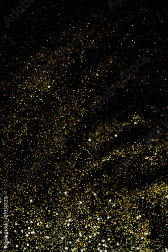 Golden glitter scattered on the black card background, top view. Abstract pattern created by hand, imitaion of storm, selective focus