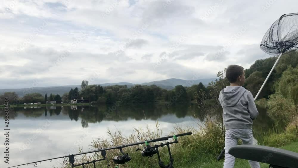 Boy holding fishing net. Beautiful fish pond near Badin, Banska Bystrica, Slovakia. Fishing place. Clouds over the lake. Mirror reflection in standing water. Little fisherman. Boy holding fishing net. Beautiful fish pond near Badin, Banska Bystrica, Slovakia. Fishing place. Clouds over the lake. Mirror reflection in standing water. Little fisherman.