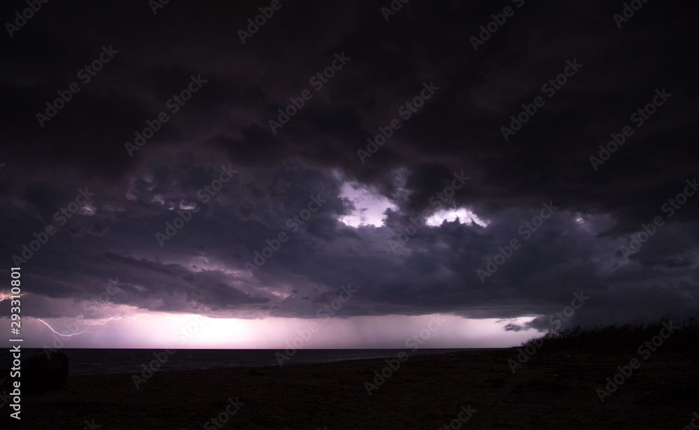 Massive thunderstorm with black cloud over the sea and lightings on the horizon