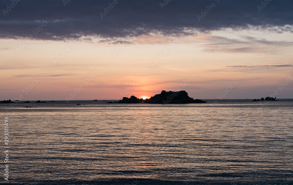sunset at the beach with a calm ocean and rocks and reefs under an orange and blue sky
