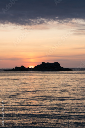 sunset at the beach with a calm ocean and rocks and reefs under an orange and blue sky