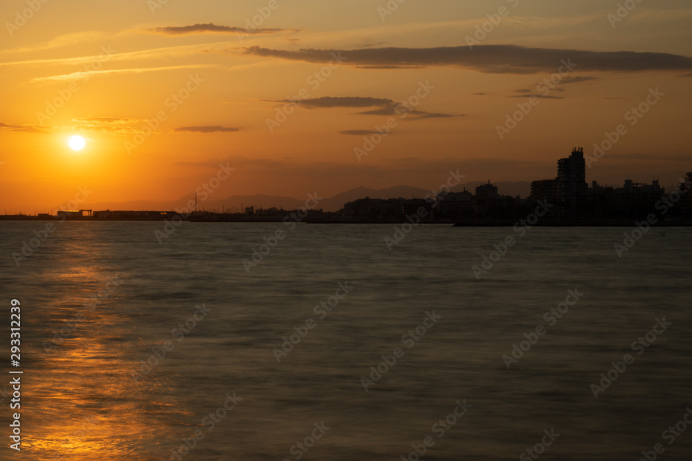 Atardecer en Santa Pola, Alicante, España. Primer plano de mar con reflejos de sol y horizonte de cielo naranja con nubes