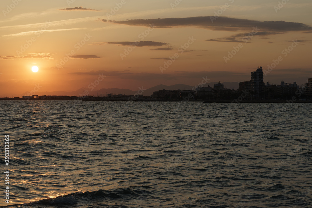 Atardecer en Santa Pola, Alicante, España. Primer plano de mar con reflejos de sol y horizonte de cielo naranja con nubes