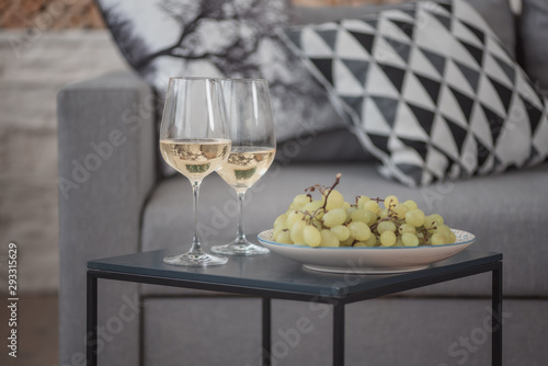 Two wine glasses, grape on plate over sofa with pillow
