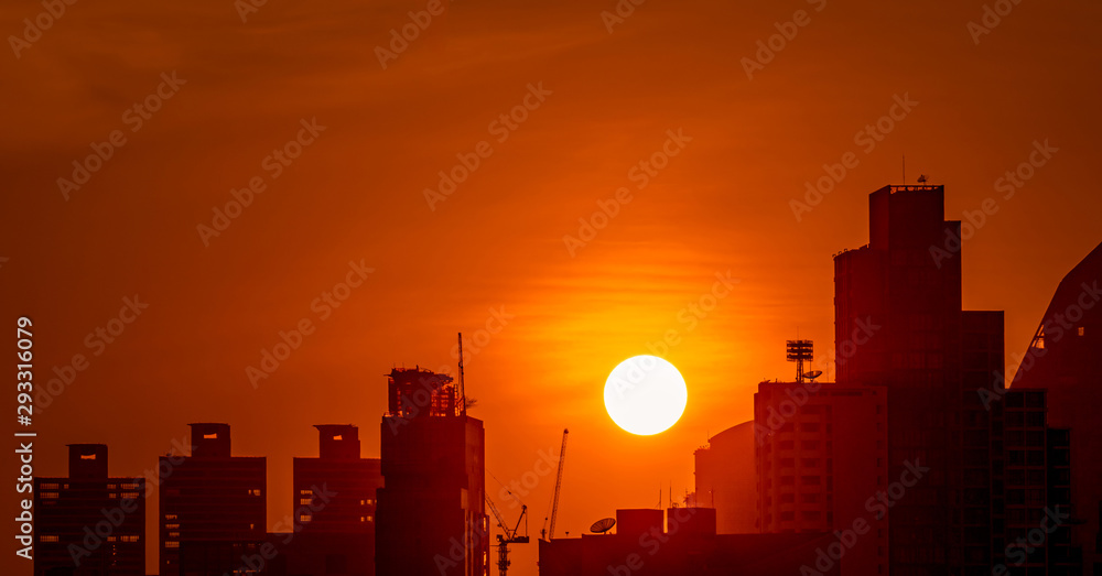 Business building in downtown at dusk with beautiful sunset sky. Silhouette of condo and apartment in the evening. Cityscape of skyscraper building and construction crane. Big sun with red sky.