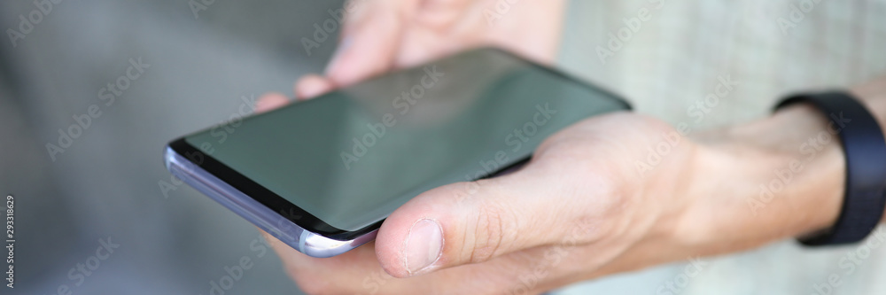 Focus on high-tech smartphone in male hands used to wireless communication. Trendy person with smart watch holding gadget with blank display. Copy space on empty screen. Blurred background