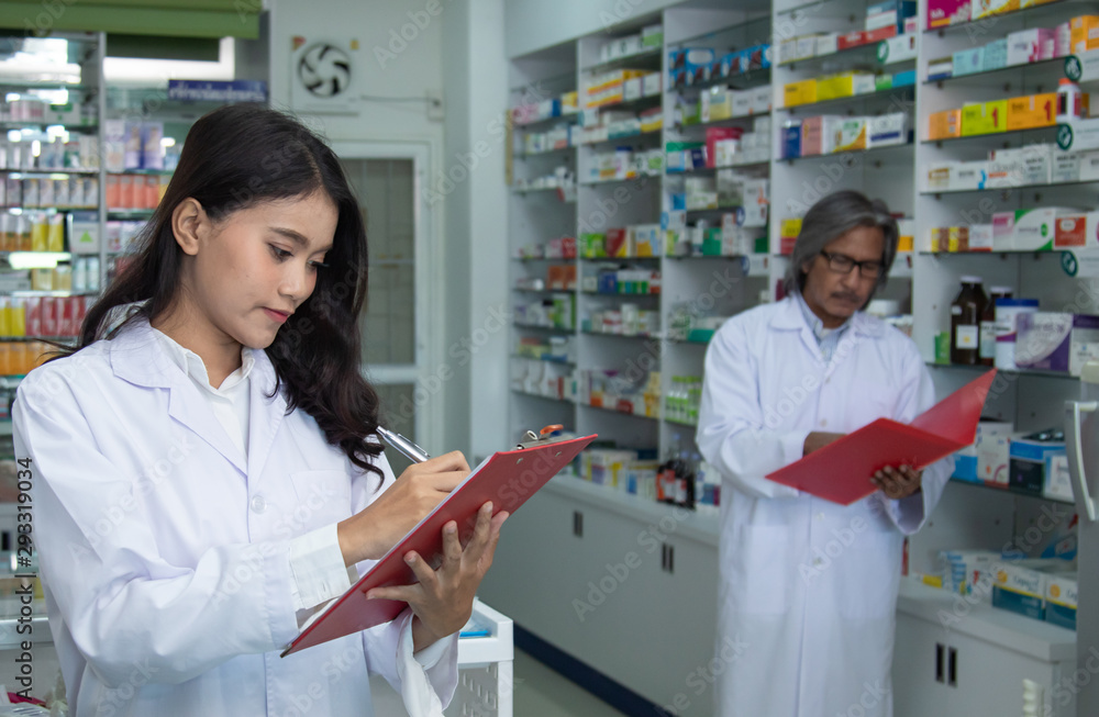 Team pharmacists colleague concentrate with pills senior man with blonde hair apothecary advice or discussing medicines with young Asian attractive colleague in drugstore blurred background