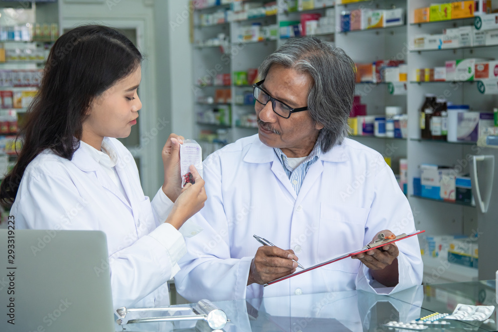 Team pharmacists colleague concentrate with pills senior man with blonde hair apothecary advice or discussing medicines with young Asian attractive colleague in drugstore blurred background Team pharmacists colleague concentrate with pills senior man with blonde hair apothecary advice or discussing medicines with young Asian attractive colleague in drugstore blurred background