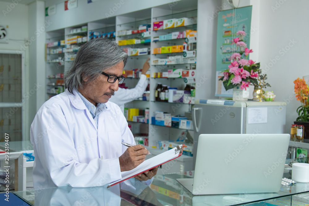 Team pharmacists colleague concentrate with pills senior man with blonde hair consulting advice or discussing medicines with young Asian attractive colleague in drugstore blurred background