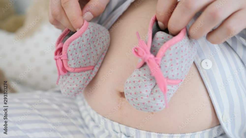 Close-Up Of Pregnant Woman Holding Baby Booties On Her Belly. Close-Up Of Pregnant Woman Holding Baby Booties On Her Belly.