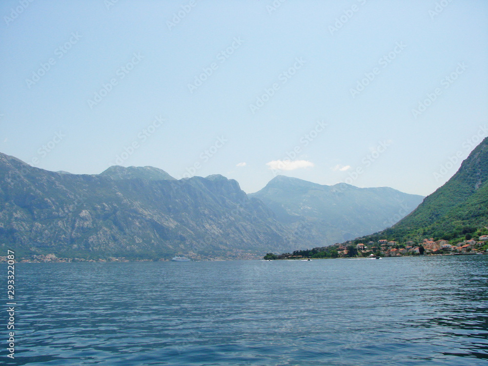 Landscape of the water surface of the calm bay on the background of rocky ridges and clear summer sky.