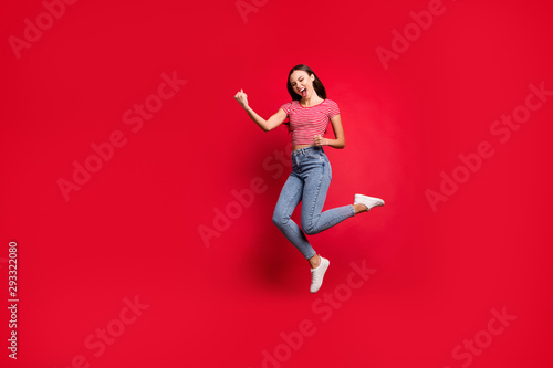 Full length body size photo charming cute fascinating nice girlfriend wearing jeans denim striped t-shirt winning something and rejoicing with it while isolated with red background