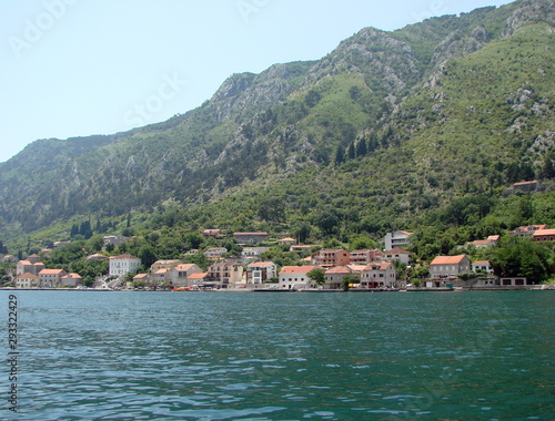 Panorama from the sea of ​​Montenegrin coastal settlements at the foot of steep cliffs covered with poor vegetation against a background of blue sky.