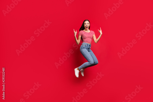 Full length body size photo of trendy cheerful shouting woman grimacing wearing jeans denim striped t-shirt footwear sneakers hard rock fan while isolated with red background