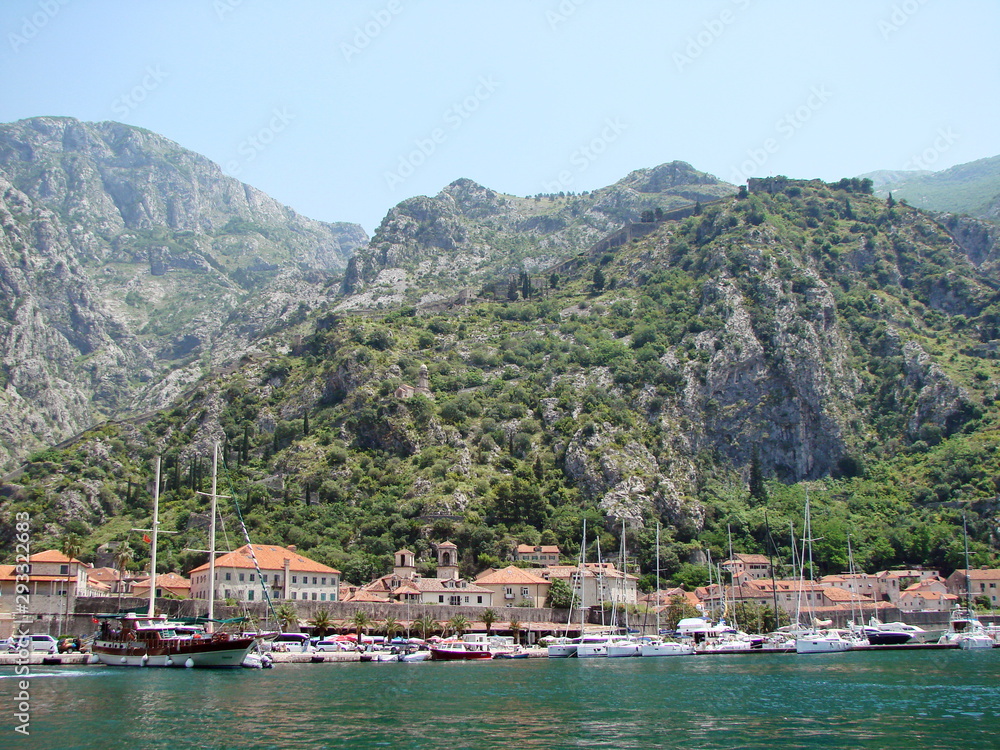 Panorama from the sea of ​​Montenegrin coastal settlements at the foot of steep cliffs covered with poor vegetation against a background of blue sky.