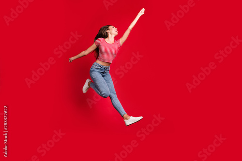 Full length body size photo of beautiful crazy cute stretching up to reach something while wearing jeans trendy denim striped t-shirt footwear while isolated with red background