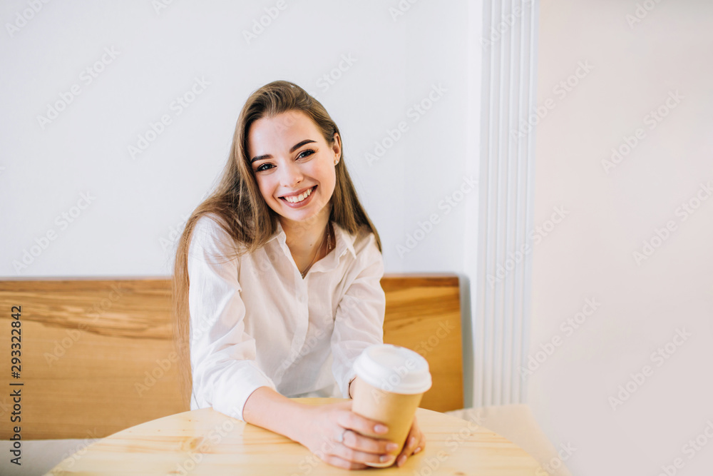 Young happy woman with long hair is sitting at the table in a cafe with a cup of coffee smiling. Young happy woman with long hair is sitting at the table in a cafe with a cup of coffee smiling.