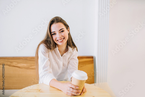 Young happy woman with long hair is sitting at the table in a cafe with a cup of coffee smiling.