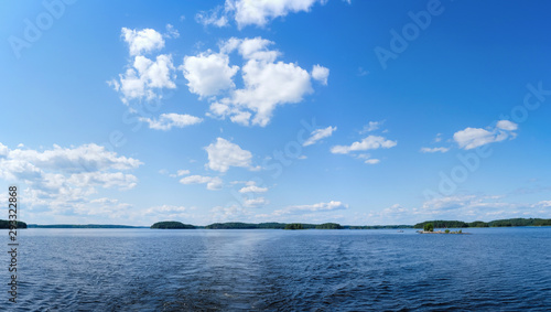 Back view of motor boat cruising on calm water, overlooking islands and blue sky. Lake Saimaa, Finland.