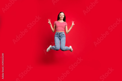 Full length body size photo of charming cute beautiful pretty girlfriend wearing jeans denim jumping with happiness while isolated over red background