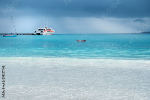 Fototapeta Naklejka Na Ścianę i Meble -  Beautiful light at the horizon on a rainy day at Kuto Bay with a ferry boat at the pier on Isle of Pines in New Caledonia, French Polynesia, South Pacific Ocean.