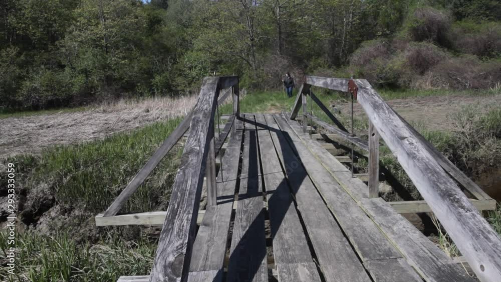 Location shot of an active overweight woman hiking with a walking stick toward the camera while crossing a small foot bridge Location shot of an active overweight woman hiking with a walking stick toward the camera while crossing a small foot bridge