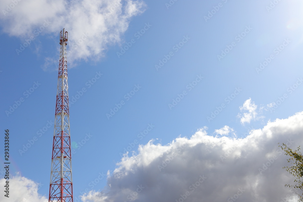 Telecommunications tower on light blue sky background and white club clouds