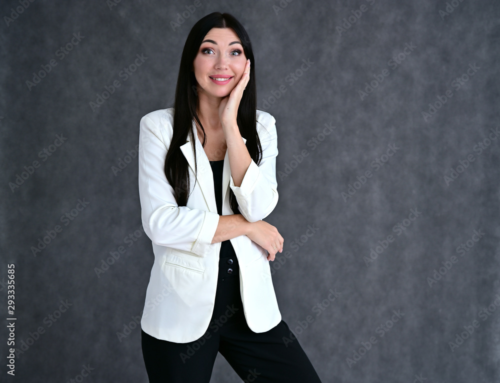 Portrait of a pretty brunette girl with good makeup with long hair on a gray background in a light business suit. Stands in different poses with emotions. Portrait of a pretty brunette girl with good makeup with long hair on a gray background in a light business suit. Stands in different poses with emotions.
