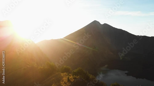 Aerial drone panning shot of a lake surrounded by mountains sun flares coming from between the mountains in Mount Rinjani, Lombok, Indonesia photo