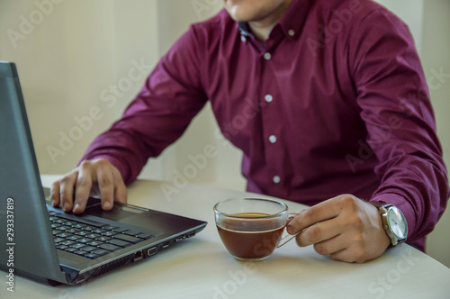A man businessman working behind a laptop and drinking coffee. Work in the office. Business. Freelancer. Work at home.