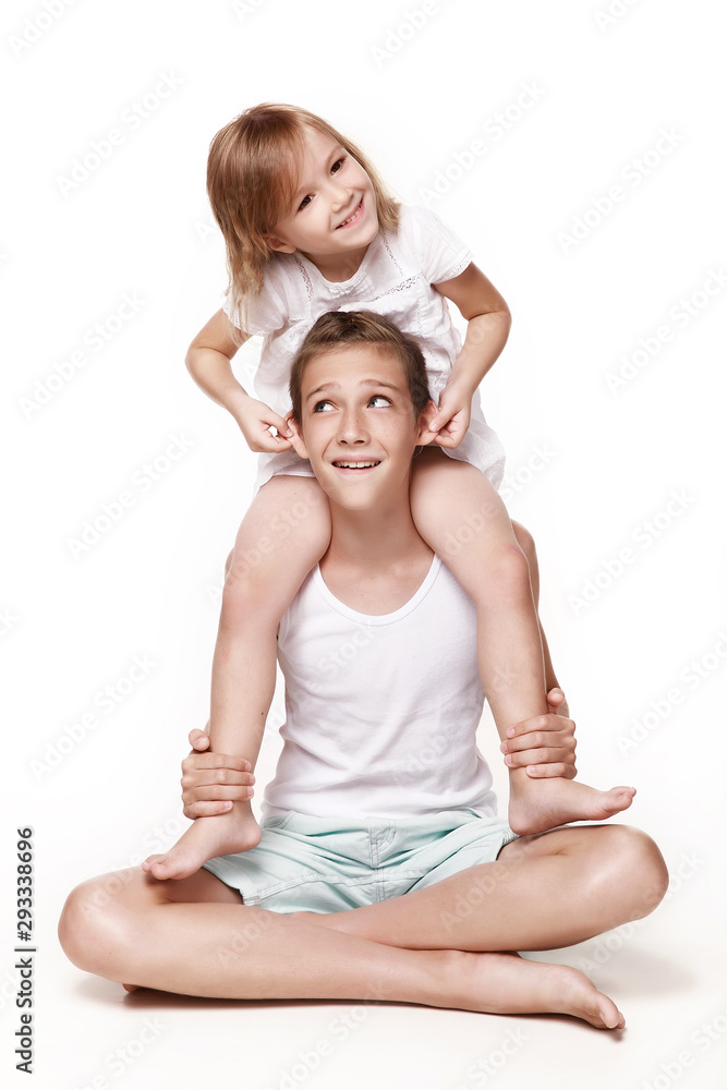 The sister sits on her brother 's neck and pulls his hands by his ears,  everyone laughs, pampers, plays together. In the studio on a white  background. Happy childhood. Stock Photo