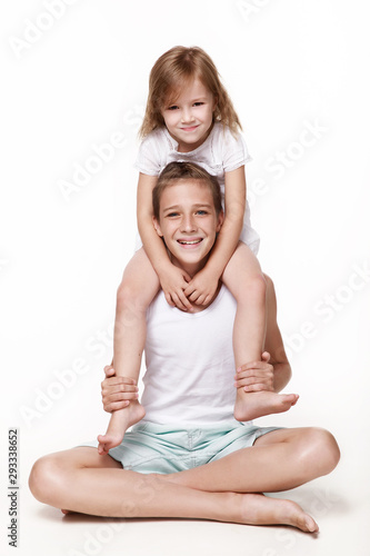 The sister sits on her brother 's neck, everyone laughs, pampers, plays together. In the studio on a white background. Happy childhood. photo