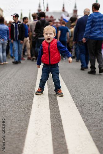 Toddler screaming while standing on a dividing strip on the road, with many people behind