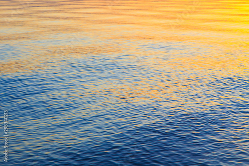 Clear water texture in blue and orange. Background of the ocean and the sea backlit by the sun. Soft waves. Natural water